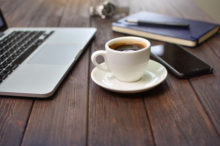 A coffee cup with a laptop and other work supplies on a table