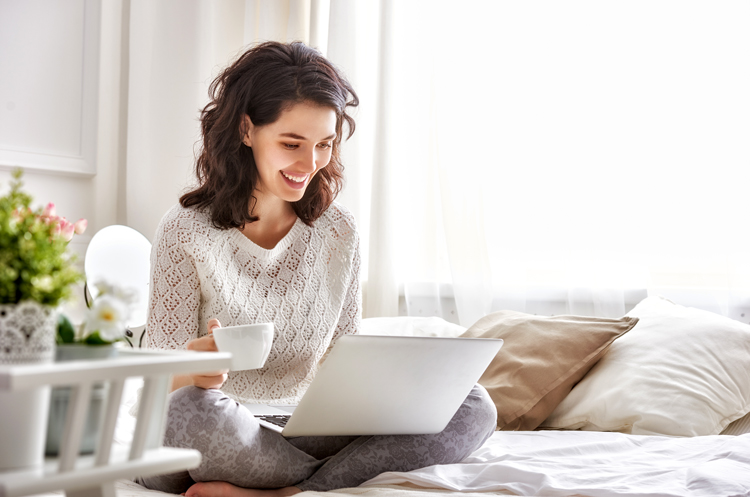 Woman sits on daybed looking at laptop