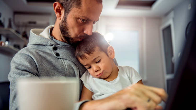 man working at laptop while holding a child