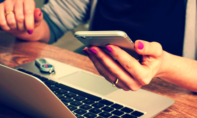 A person holding a cellphone while working on a laptop